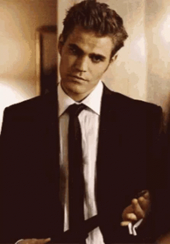 A Man In A Suit And Tie Is Smoking A Cigarette While Standing In A Room . GIF