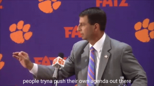 a man in a suit and tie is speaking into a microphone in front of a clemson banner