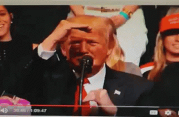 A Man In A Suit And Tie Is Speaking Into A Microphone In Front Of A Crowd GIF