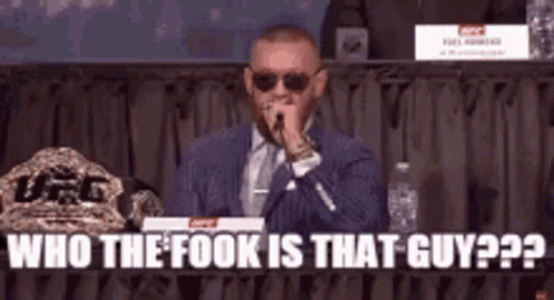 A Man In A Suit And Tie Is Speaking Into A Microphone While Sitting At A Table . GIF
