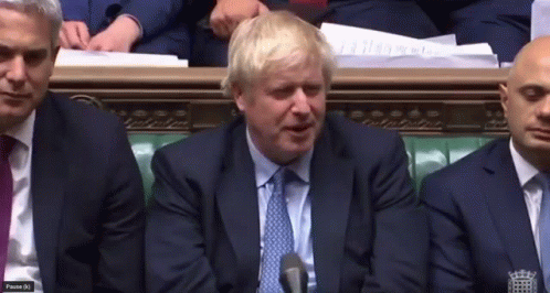 A Man In A Suit And Tie Is Speaking Into A Microphone While Sitting In A Room With Other Men GIF