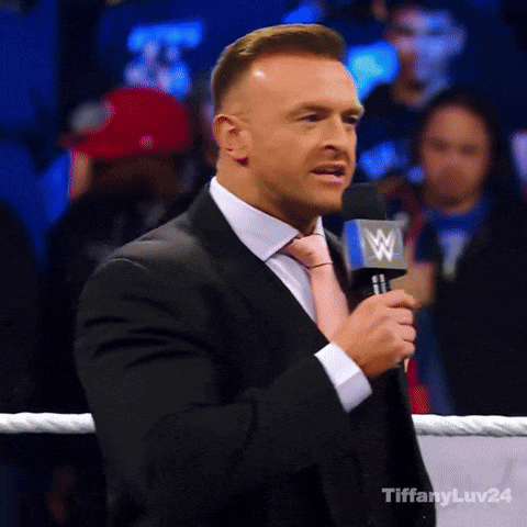 A Man In A Suit And Tie Is Speaking Into A Microphone With A W Logo On It GIF