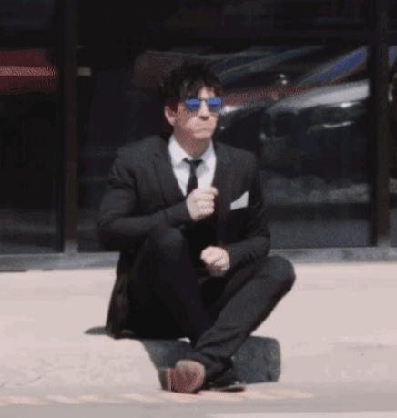 A Man In A Suit And Tie Is Squatting Down On The Ground GIF