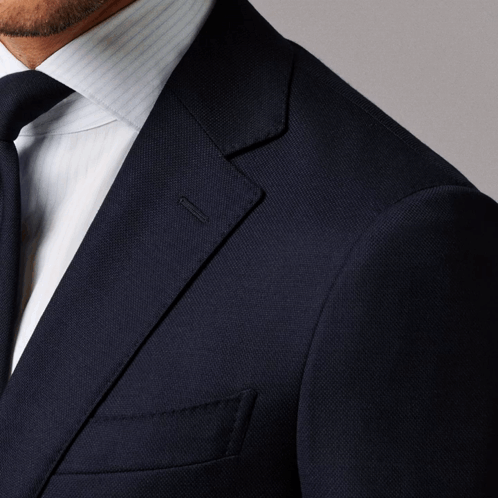 A Man In A Suit And Tie Is Standing Against A Grey Background GIF