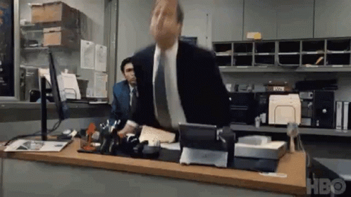 A Man In A Suit And Tie Is Standing At A Desk In An Office With A Computer . GIF