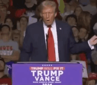 A Man In A Suit And Tie Is Standing At A Podium Giving A Speech In Front Of A Crowd . GIF