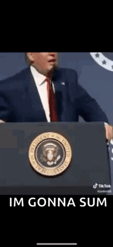 A Man In A Suit And Tie Is Standing At A Podium With The Words `` Im Gonna Sum '' Below Him . GIF