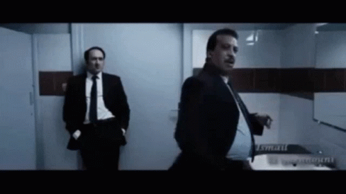 A Man In A Suit And Tie Is Standing In A Bathroom GIF