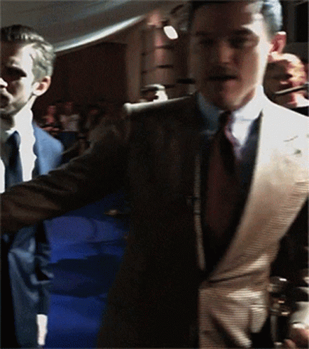 A Man In A Suit And Tie Is Standing In A Crowd GIF