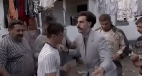 A Man In A Suit And Tie Is Standing In A Crowd Of Men . GIF