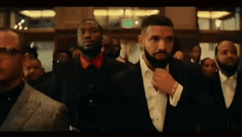 A Man In A Suit And Tie Is Standing In A Crowd Of People . GIF
