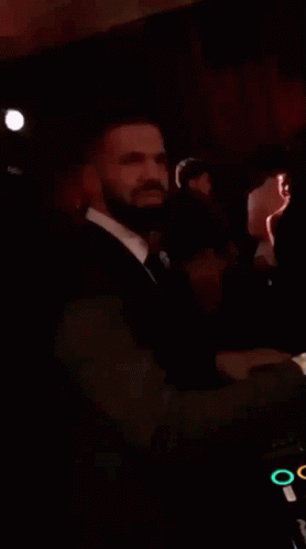 A Man In A Suit And Tie Is Standing In A Dark Room And Smiling . GIF