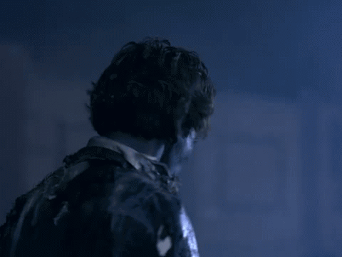 A Man In A Suit And Tie Is Standing In A Dark Room With A Blue Light Behind Him . GIF