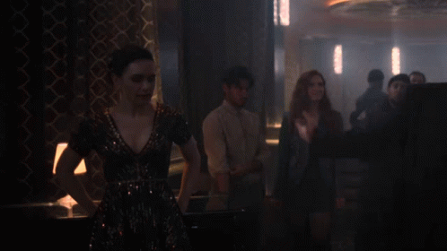 A Man In A Suit And Tie Is Standing In A Dark Room GIF
