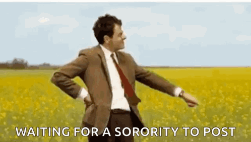 A Man In A Suit And Tie Is Standing In A Field Of Yellow Flowers And Waiting For A Sorority To Post . GIF