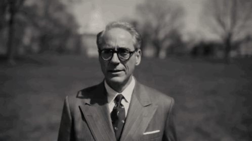 A Man In A Suit And Tie Is Standing In A Grassy Field . GIF