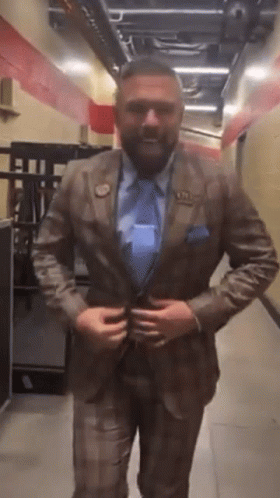 A Man In A Suit And Tie Is Standing In A Hallway Adjusting His Jacket GIF