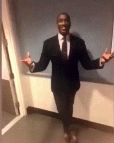 A Man In A Suit And Tie Is Standing In A Hallway . GIF