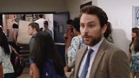 A Man In A Suit And Tie Is Standing In A Hallway Surrounded By Students . GIF