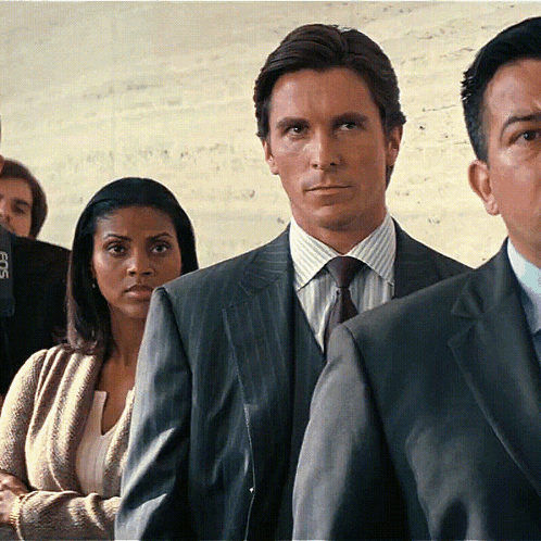 A Man In A Suit And Tie Is Standing In A Line With Other People GIF