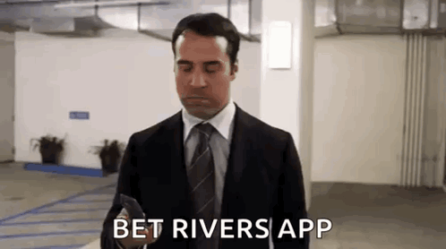 A Man In A Suit And Tie Is Standing In A Parking Garage And Looking At His Phone . GIF