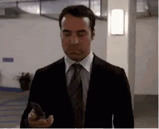 A Man In A Suit And Tie Is Standing In A Parking Garage Holding A Cell Phone . GIF