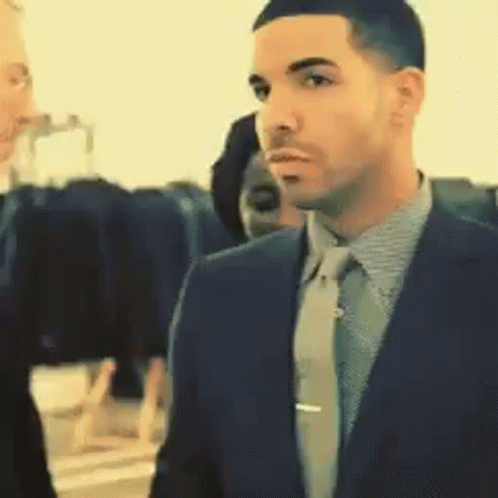 A Man In A Suit And Tie Is Standing In A Room GIF