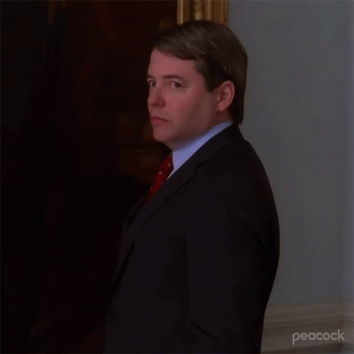 A Man In A Suit And Tie Is Standing In A Room . GIF