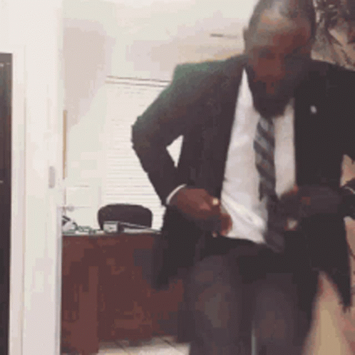 A Man In A Suit And Tie Is Standing In A Room . GIF