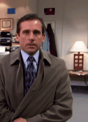 A Man In A Suit And Tie Is Standing In A Room With A Lamp GIF