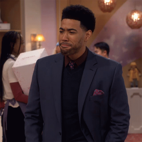 A Man In A Suit And Tie Is Standing In A Room With A Woman Behind Him GIF