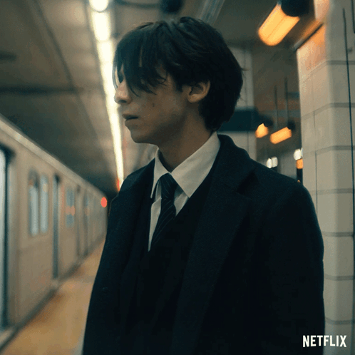 A Man In A Suit And Tie Is Standing In A Subway Station With A Netflix Logo Behind Him GIF