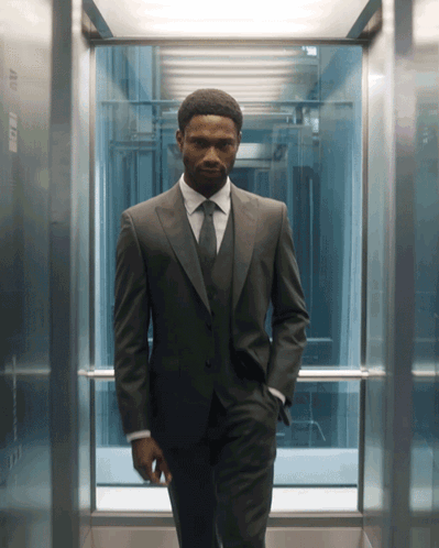 A Man In A Suit And Tie Is Standing In An Elevator With His Hands In His Pockets GIF