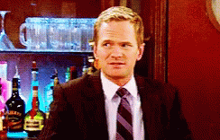 A Man In A Suit And Tie Is Standing In Front Of A Bar Full Of Bottles GIF