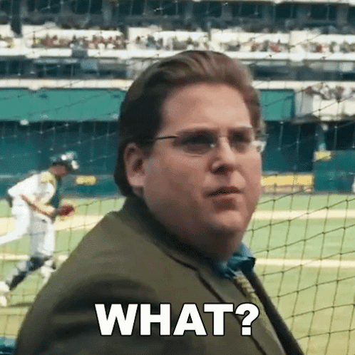 A Man In A Suit And Tie Is Standing In Front Of A Baseball Field And Asking What ? GIF