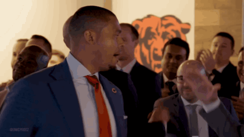 A Man In A Suit And Tie Is Standing In Front Of A Bears Logo GIF
