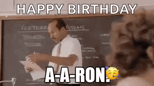 A Man In A Suit And Tie Is Standing In Front Of A Blackboard And Holding A Piece Of Paper . GIF