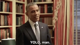 A Man In A Suit And Tie Is Standing In Front Of A Bookshelf And Says " Yolo , Man " . GIF