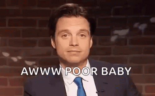 A Man In A Suit And Tie Is Standing In Front Of A Brick Wall And Talking Into A Microphone . GIF