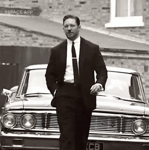 A Man In A Suit And Tie Is Standing In Front Of A Car . GIF