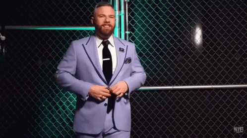 A Man In A Suit And Tie Is Standing In Front Of A Chain Link Fence GIF
