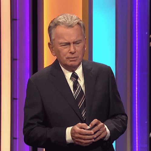 A Man In A Suit And Tie Is Standing In Front Of A Colorful Wall GIF