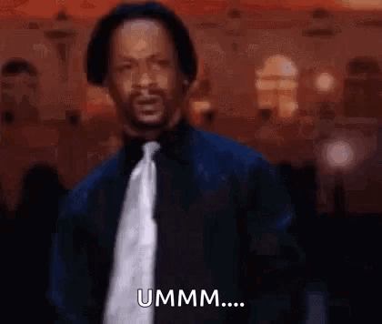 A Man In A Suit And Tie Is Standing In Front Of A Crowd And Saying Ummm . GIF