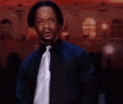 A Man In A Suit And Tie Is Standing In Front Of A Crowd In A Room . GIF