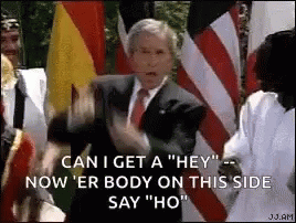 A Man In A Suit And Tie Is Standing In Front Of A Crowd Of People And Flags . GIF