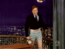 A Man In A Suit And Tie Is Standing In Front Of A Curtain That Says Nbc GIF