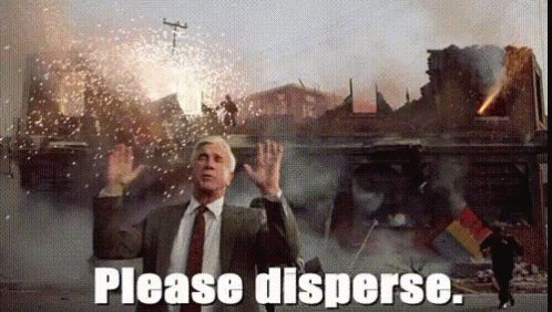 A Man In A Suit And Tie Is Standing In Front Of A Destroyed Building And Says Please Disperse GIF