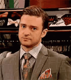 A Man In A Suit And Tie Is Standing In Front Of A Display Of Ties . GIF