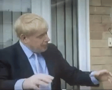 A Man In A Suit And Tie Is Standing In Front Of A Door And Talking On A Cell Phone . GIF