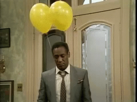 a man in a suit and tie is standing in front of a door with two yellow balloons hanging from it .